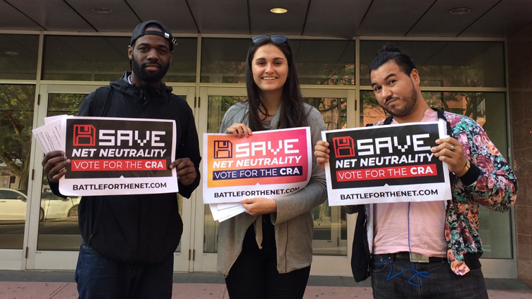 Three Net Neutrality activists holding signs reading “Save Net Neutrality. Vote for the CRA.”